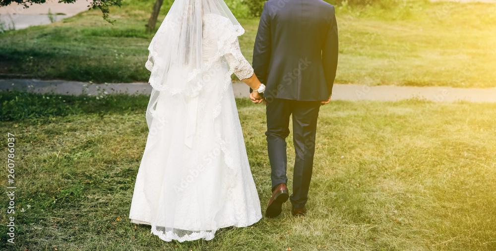 Wedding couple walking in the green park. Curvy bride in white lace dress and groom are holding hands. Overweight happy people. Love story outdoors. Beautiful bouquet.