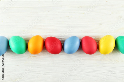 Bunch of blank painted Easter eggs of different pastel color on white wood textured table background with a lot of copy space for text. Top view, flat lay, close up.