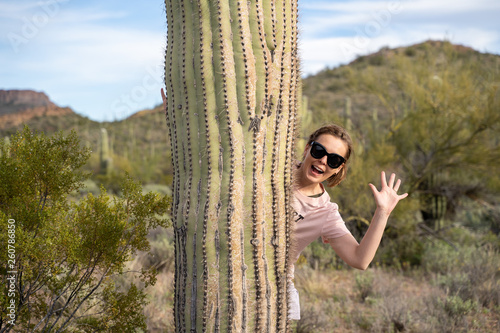 Adult woman hides and waves while standing behind a large saguaro cactus in the Sonoran Desert photo