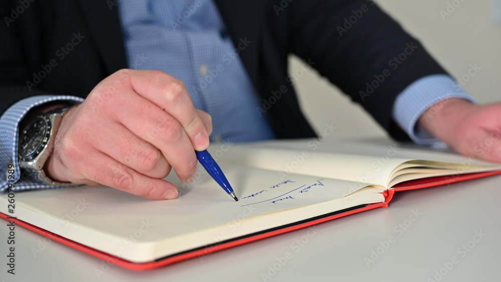 Mann schreibt mit blauem Stift in ein Notizbuch Mann schreibt mit blauem Stift in ein Notizbuch