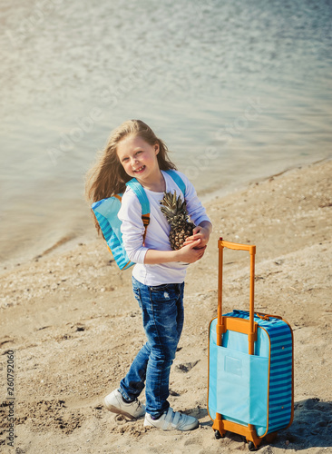 Cute little girl with suitecase on the beach. Summertime concept.