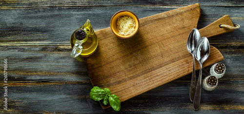 banner of Cutting wooden board from olive wood on a blue wooden table with olive oil, basil and Parmesan cheese. Mediterranean table settingn board from olive wood on a blue wooden table  photo
