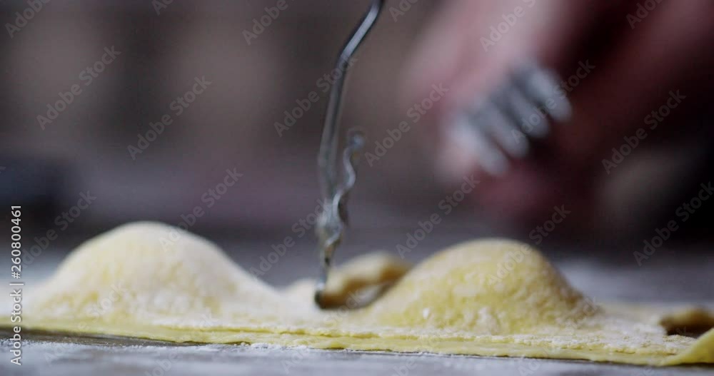 Fresh homemade ravioli pasta shapes are cut using a traditional wheel cutter. A hand picks up the ravioli once it is cut. Fresh homemade ravioli pasta shapes are cut using a traditional wheel cutter. A hand picks up the ravioli once it is cut.