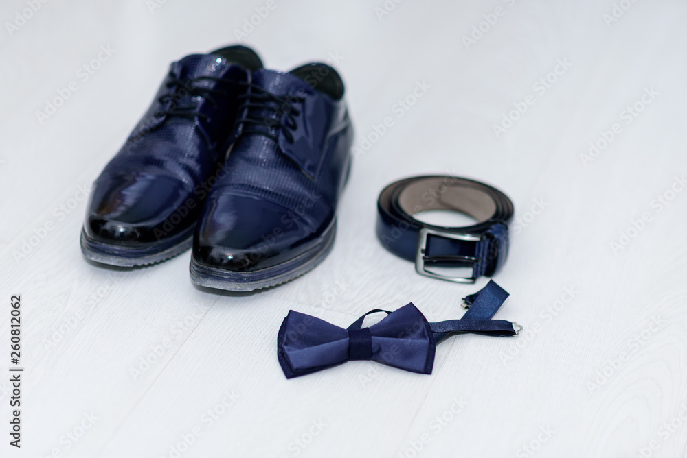Close up of modern man accessories. Bow tie, dark blue leather shoes, belt on white background. Set for formal style of wearing isolated on white background. Close up of modern man accessories. Bow tie, dark blue leather shoes, belt on white background. Set for formal style of wearing isolated on white background.