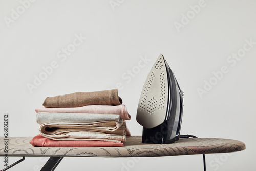 Fotografie Iron and folded ironed clothes on ironing board isolated on grey