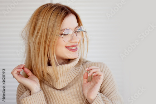 Stylish and beautiful young blonde in beige oversize sweater. Young woman with glasses