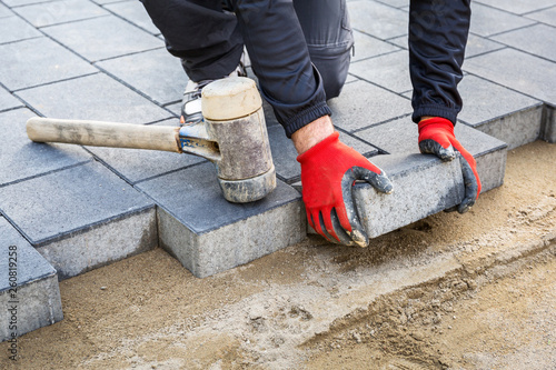Hands of worker installing concrete paver blocks with rubber hammer