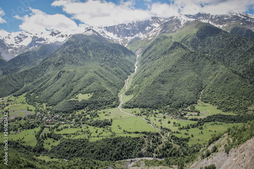 Scenic valley in the Caucasus Mountains with a small village  summer greens and snow-capped peaks