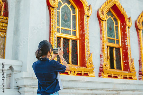 Asian woman travelers from behind taking ancient temple buildings photos in the ancient temple scene background with copy space- Bangkok- Thailand © kintarapong