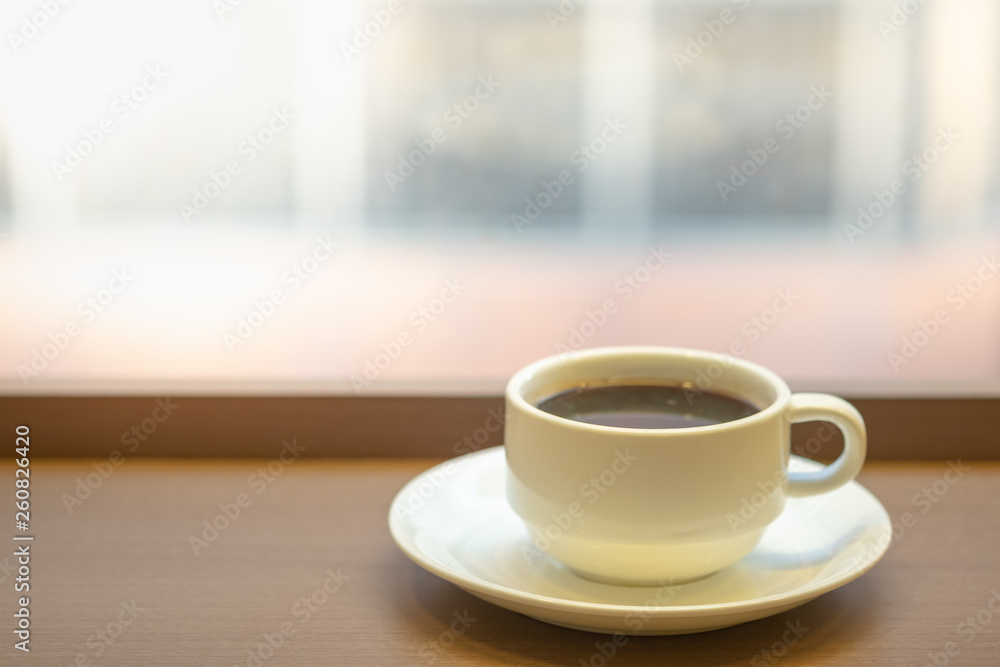 Close up of white mug cup of hot black coffee on wooden table.