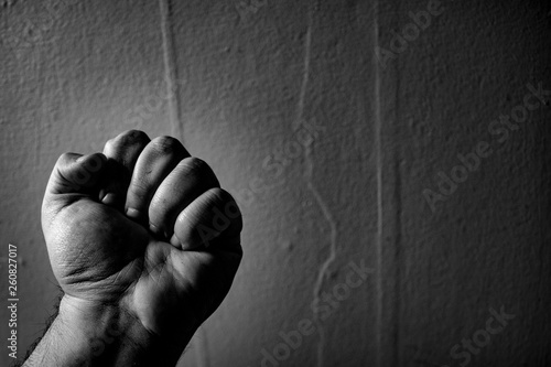 An aggressive monochrome adult male clenched fist isolated on a black background.