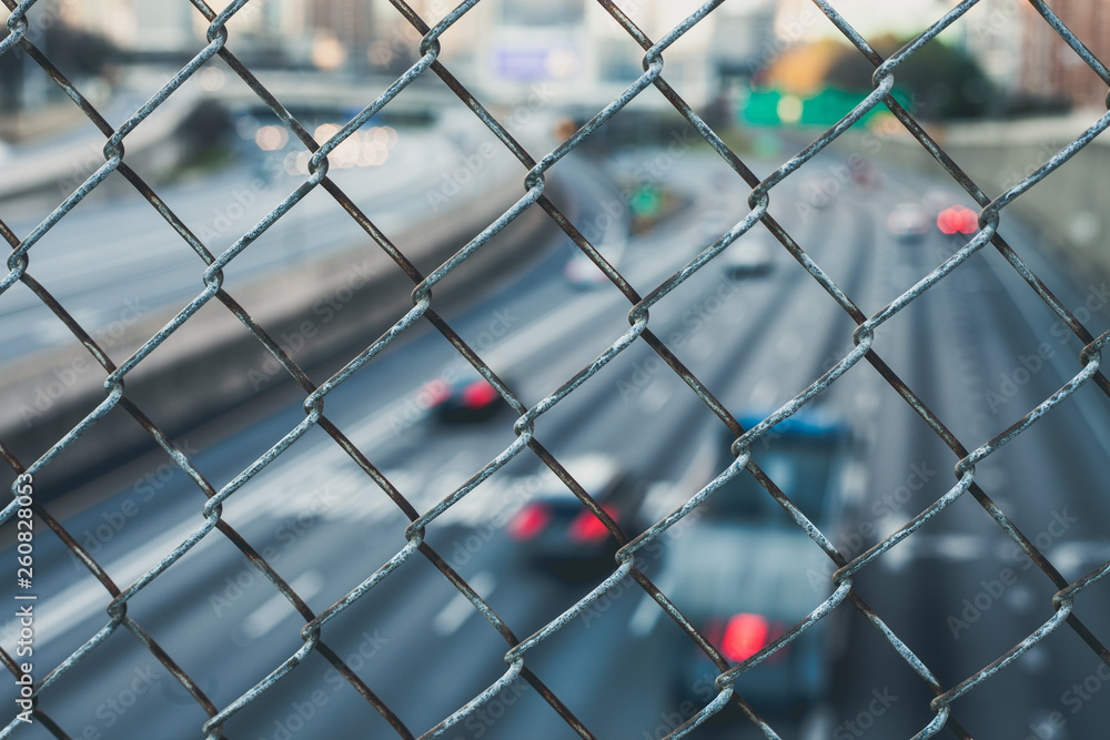 Fototapeta premium City skyline through the wire mesh fence. Abstract blurred cityscape background