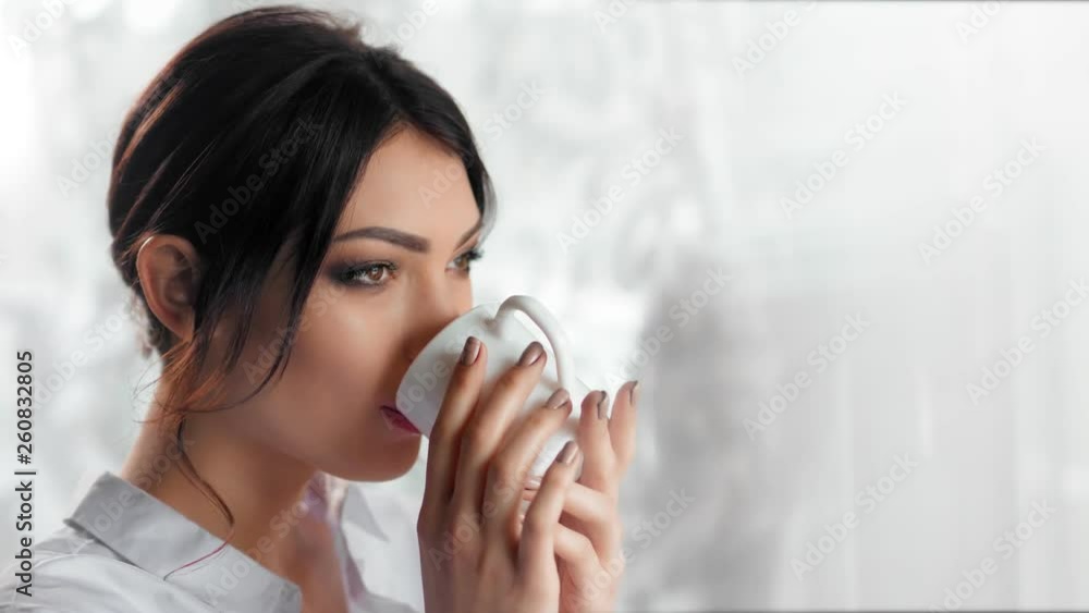 Medium close-up happy pleasant young woman drinking coffee or tea holding white mug Medium close-up happy pleasant young woman drinking coffee or tea holding white mug