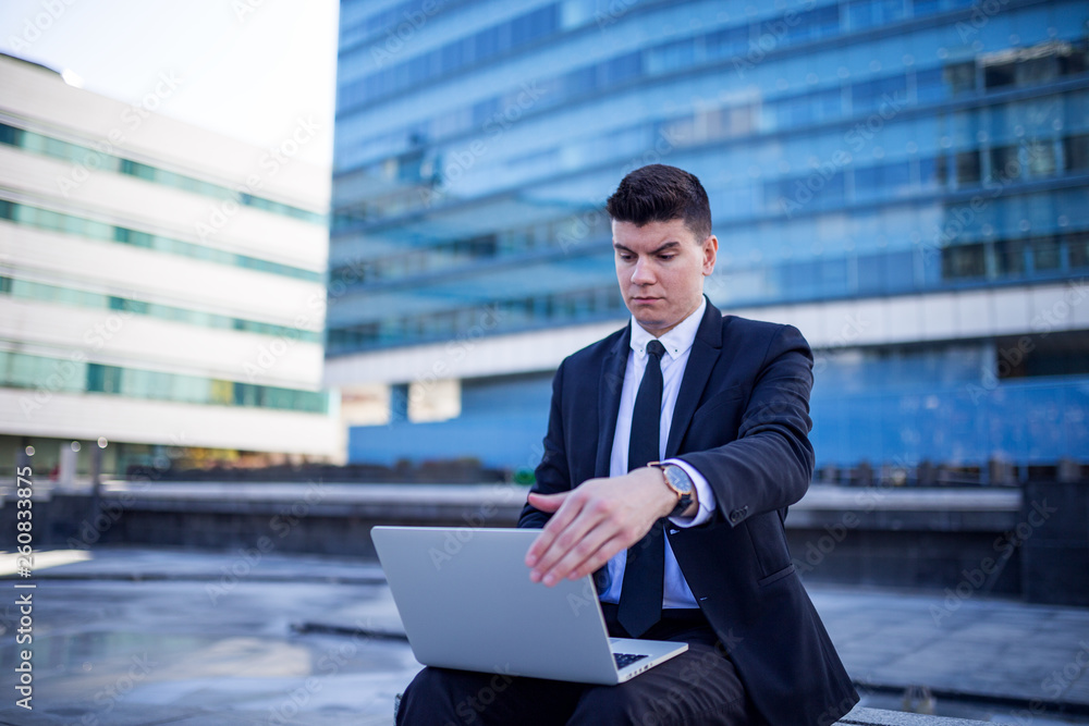 Confident young businessman using laptop in a front of building Confident young businessman using laptop in a front of building