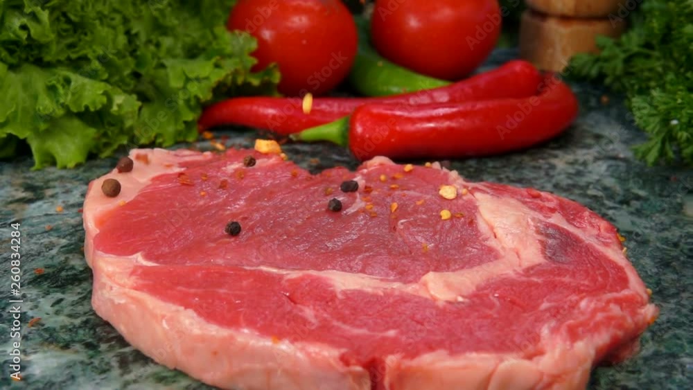 Mixture of spices falls on the veal steak in slow motion. Still life of meat, herbs, spices and vegetables Mixture of spices falls on the veal steak in slow motion. Still life of meat, herbs, spices and vegetables