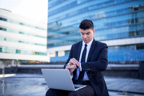Confident young businessman using laptop in a front of building
