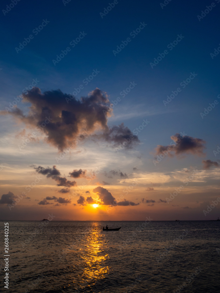 Silhouettes of people in a kayak in the rays of the setting sun against the background of clouds. Ko Phangan.Thailand.