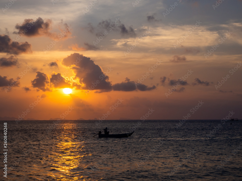 Silhouettes of people in a kayak in the rays of the setting sun against the background of clouds. Ko Phangan.Thailand.