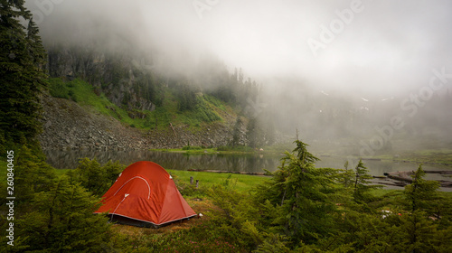 An orange tent set up next to foggy mountain lake