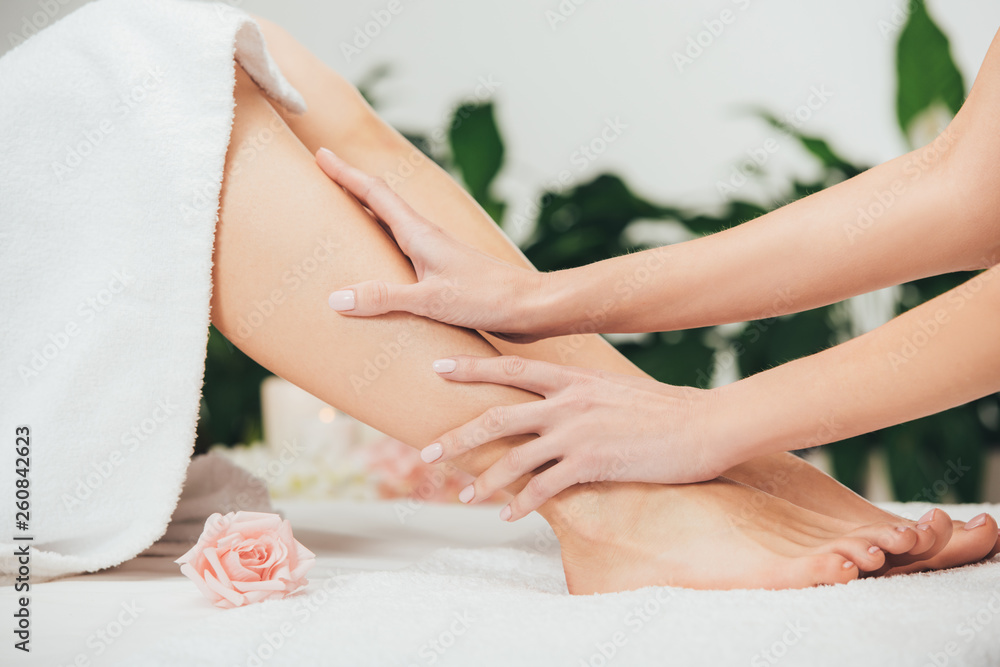 Naklejka premium partial view of masseur doing foot massage to adult woman in spa