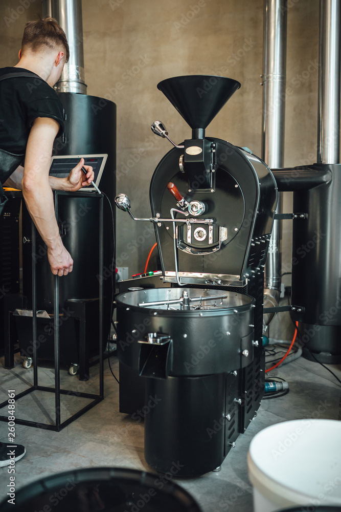 Young man coffee roaster working in roastery, coffee roasting in