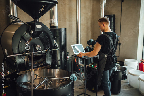 Young man coffee roaster working in roastery, coffee roasting in specialty coffee roastery.