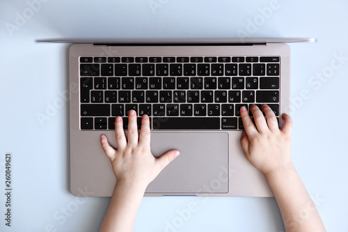 Kid hands typing on laptop keyboard on blue background, top view