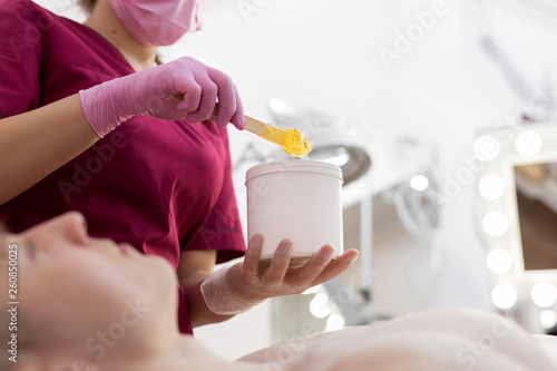 Cosmetician takes the sugar paste from the jar. Shugaring. Sugar paste out of the container with a spatula. Sugar paste for sugaring. Sugaring in beauty salon