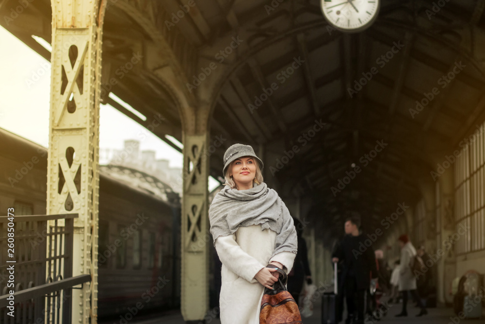 Passengers train go on the platform. Travelling by train. A woman in a white coat and hat stands on the platform. Travel concept.
