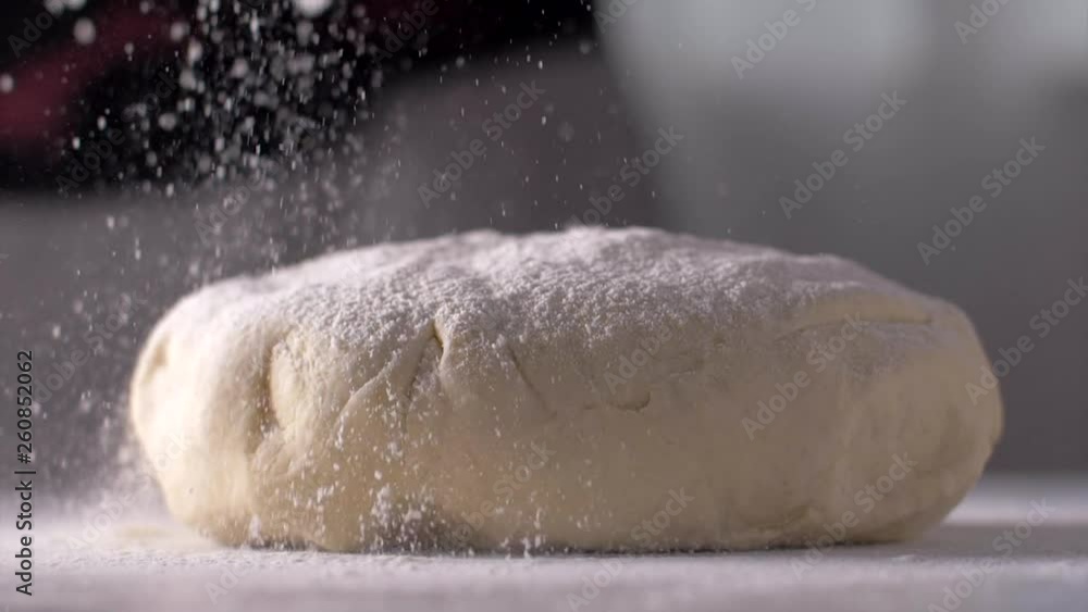 The baker sprinkles the dough with flour