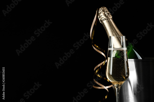 Glass of champagne near bucket with bottle on black background, space for text