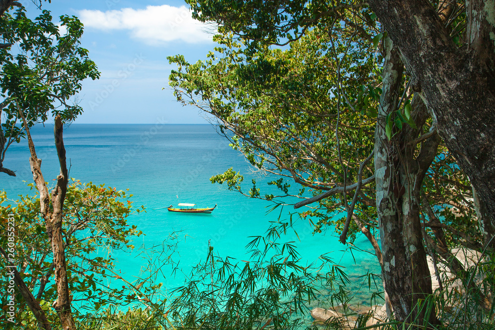 Sea view and traditional Thai boat through rainforest. Round large stones and azure clear water. Beautiful Paradise lagoon. Thailand. Andaman sea. Sea view and traditional Thai boat through rainforest. Round large stones and azure clear water. Beautiful Paradise lagoon. Thailand. Andaman sea.