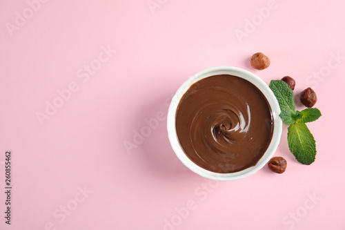 Dessert bowl with sweet chocolate cream, hazelnuts and mint on color background, top view. Space for text photo