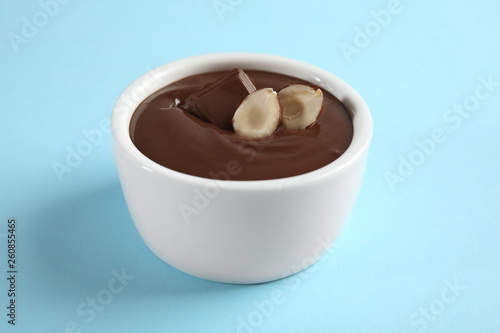 Ceramic bowl with sweet chocolate cream and hazelnuts on color background