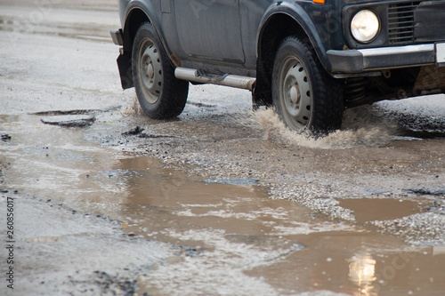 Moving car sprays puddle when heavy rain drops on concrete.