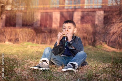 .Pre-school boy eating a hamburger sitting on a grass