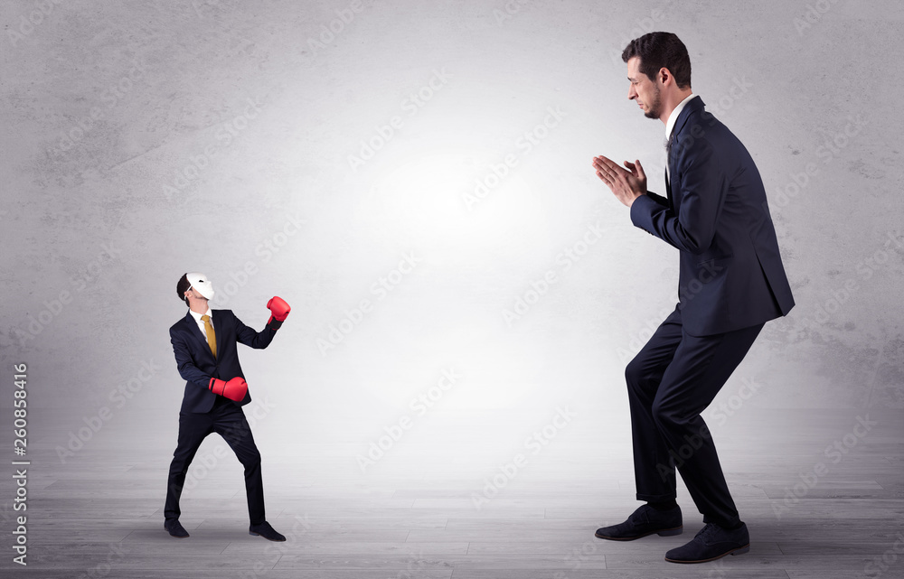 Big businessman being afraid of small masked businessman with box gloves in an empty room concept
Big businessman being afraid of small masked businessman with box gloves in an empty room concept