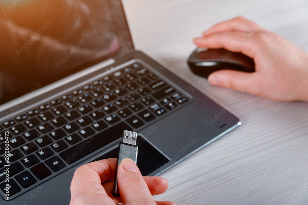 Hand of a woman holding a USB device connected to Laptop computer on white table Hand of a woman holding a USB device connected to Laptop computer on white table