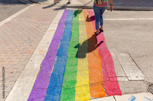 Pride colors paint covers the crosswalk. A woman crosses on the Gay Pride path of the intersection.
