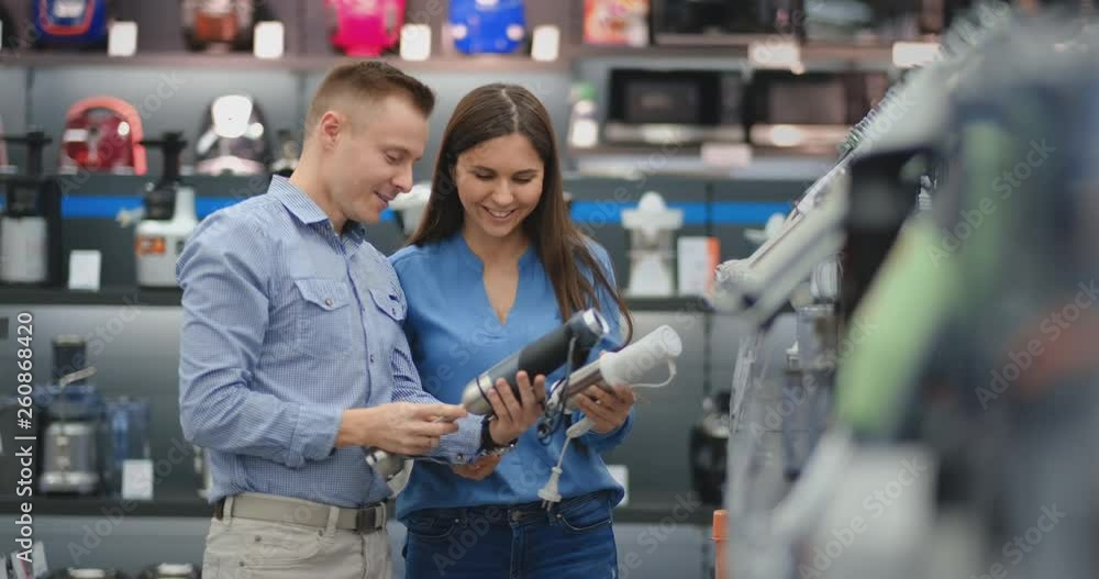 In the appliances store, a married couple in everyday clothes chooses a blender for the purchase by viewing and holding the device in their hands. In the appliances store, a married couple in everyday clothes chooses a blender for the purchase by viewing and holding the device in their hands.