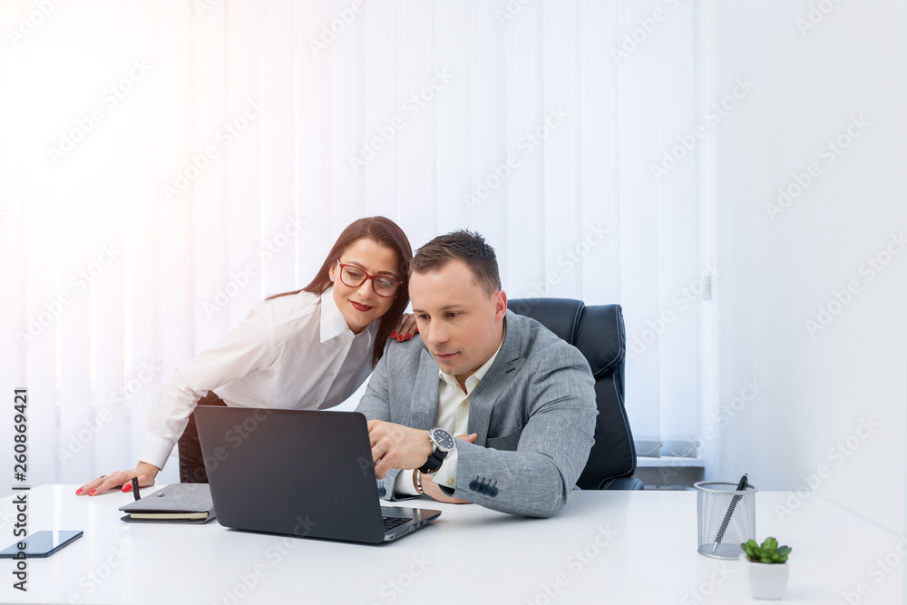 Young businessman in grey suit showing information to an attractive female coworker in modern bright office. Young businessman in grey suit showing information to an attractive female coworker in modern bright office.
