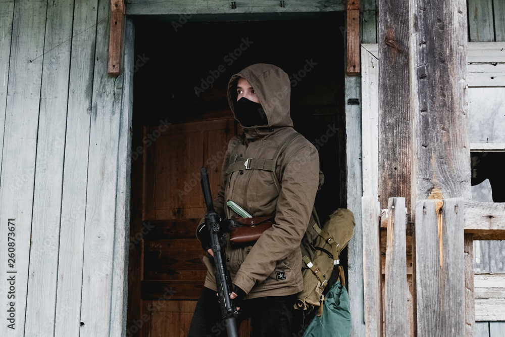 Stalker, a soldier in uniform and with a gun is standing on the porch of an old, abandoned house
