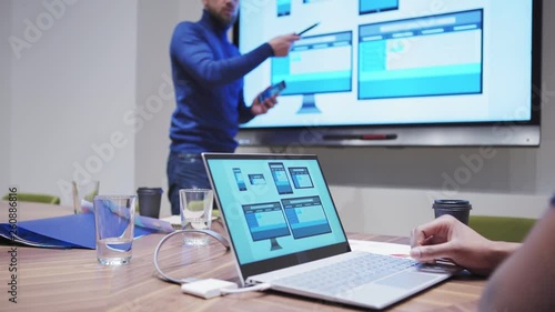 Manager presenting website design for different devices on digital board and smartphone screen, his assistant helping him magnifying slides on laptop