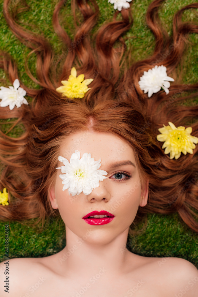 top view of beautiful young woman with red lips and chrysanthemum flowers in hair on grass