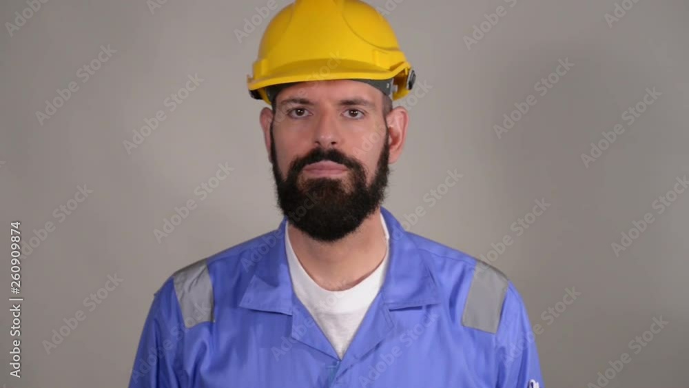 Bearded man worker in yellow helmet saluting, waving his hand over grey background Bearded man worker in yellow helmet saluting, waving his hand over grey background
