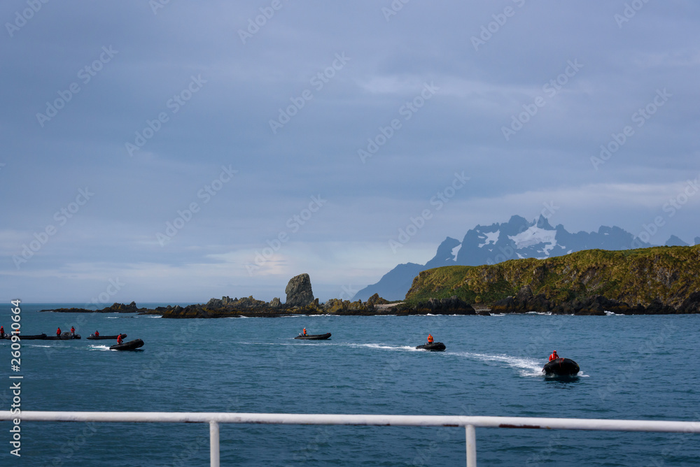 View of Coopers Bay landscape from cruise ship, fleet of inflatable rafts with drivers in red jackets getting ready to pick up tourists off ship, South Georgia, southern Atlantic Ocean