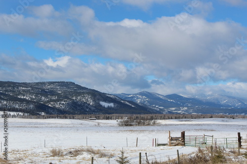 partly cloudy blue winter sky over a snowy mountain and frozen grass land and sagebrush