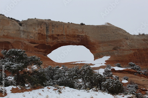 Wilson Arch , Utah. Beautiful natural archway formed out of the red stone earth of Utah, The light snow gives patches of white on the red earth and sagebrush.