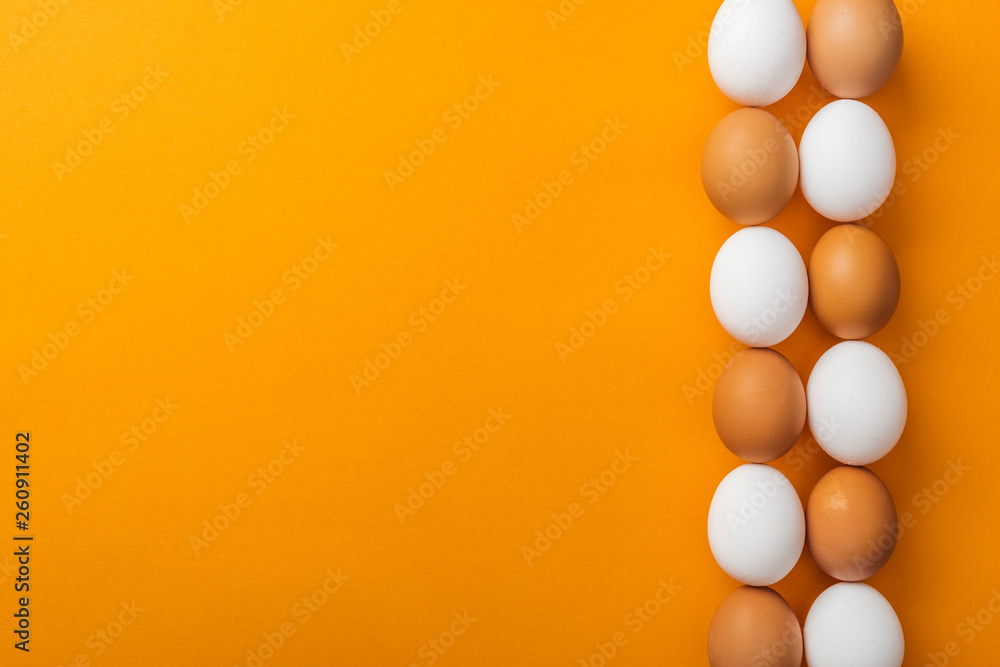 top view of white and brown organic chicken eggs on bright orange background with copy space