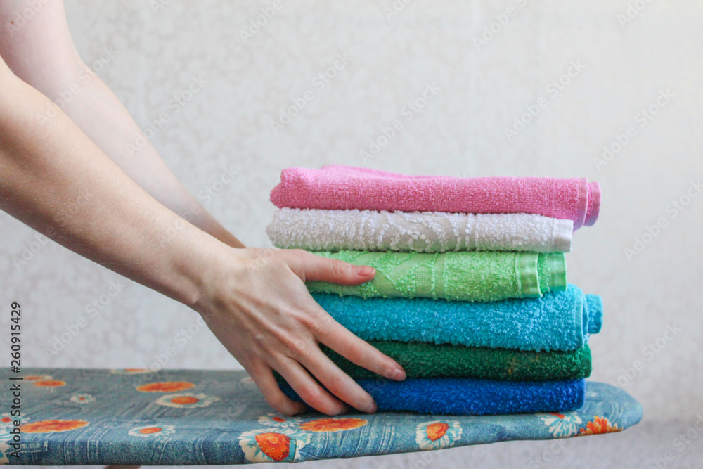 Stack of colorful clean towels on grey background. Ironing clothes on  ironing board. Stack of clean towels on table. Colored towels. Space for  text. Hygiene, fabric, laundry,spa and textile concept. Stock Photo